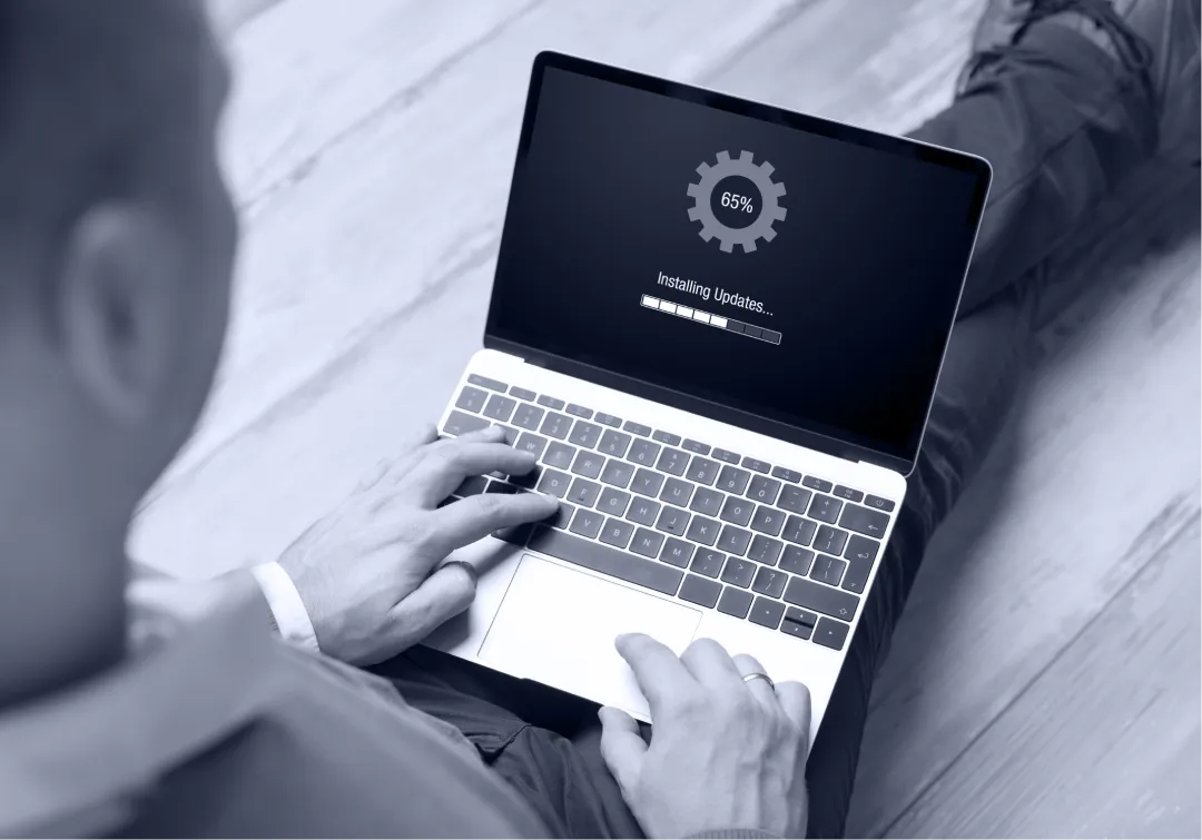 Person on a laptop showing an Installing Updates progress bar at 65 percent, tinted blue